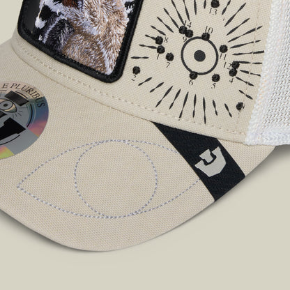 The Goorin Bros. G-Anon baseball cap in cream and black features embroidered sun dial design, animal print patches, and a black brand label, displayed in flat lay on a neutral background.