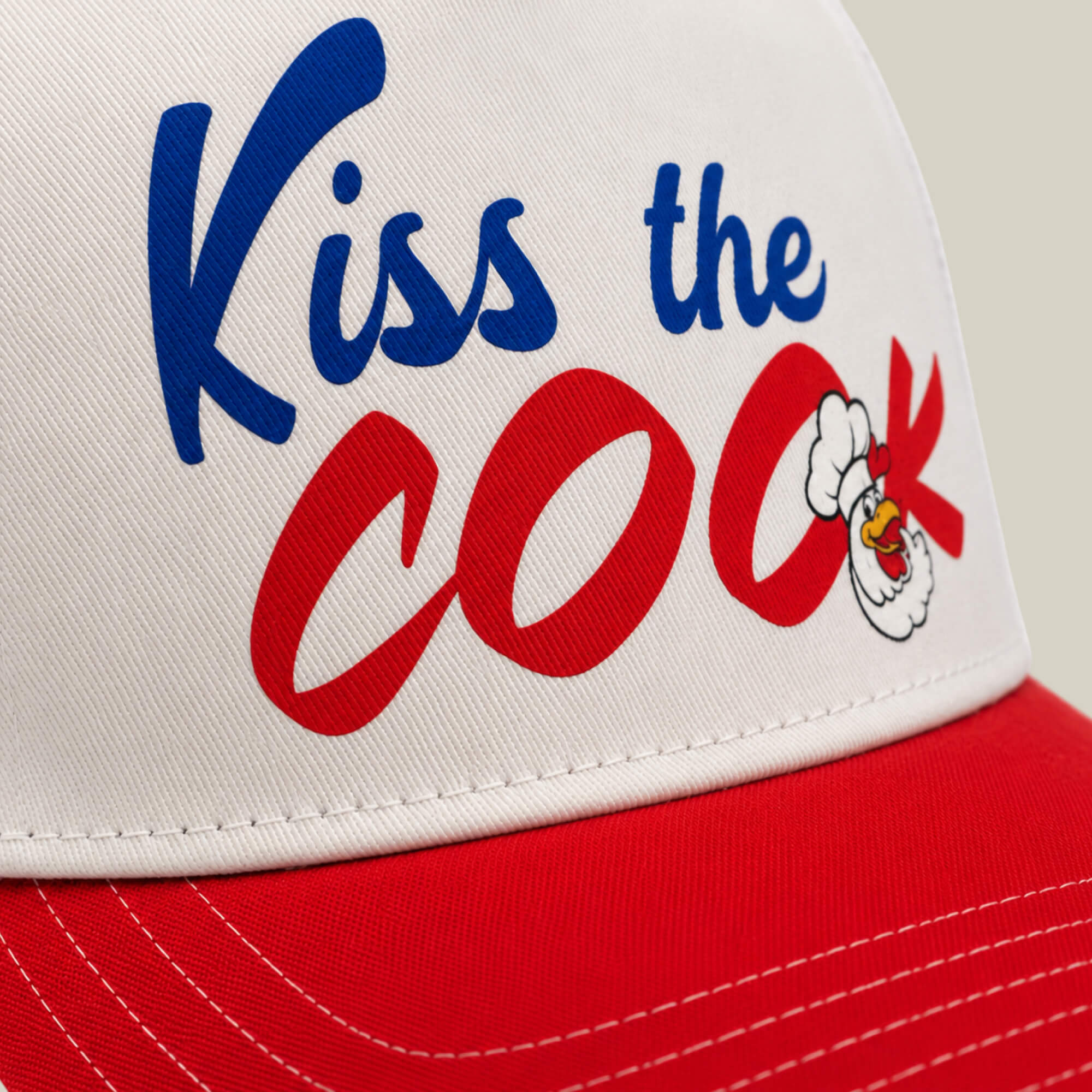 Close-up of a red and white Goorin Bros. cap called Chef's Kiss, featuring "Kiss the Cook" in blue and red letters with a cartoon chicken head—ideal for any backyard barbecue or aspiring grillmaster.