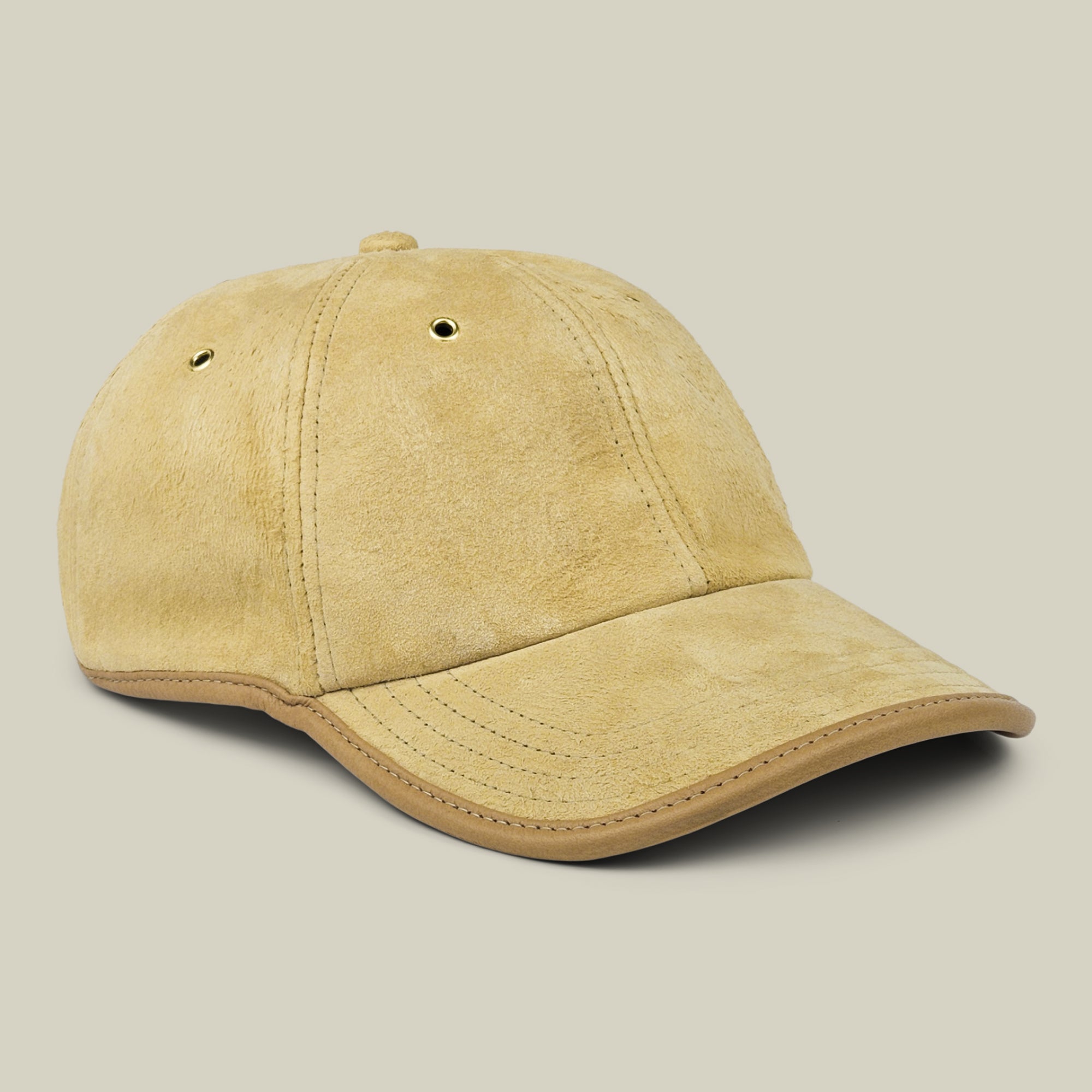 The Steiner baseball cap by Goorin Bros. is crafted from tan suede with prominent stitching and two metal eyelets on each side, and features an adjustable plaid strap at the back. It is displayed against a neutral beige background.