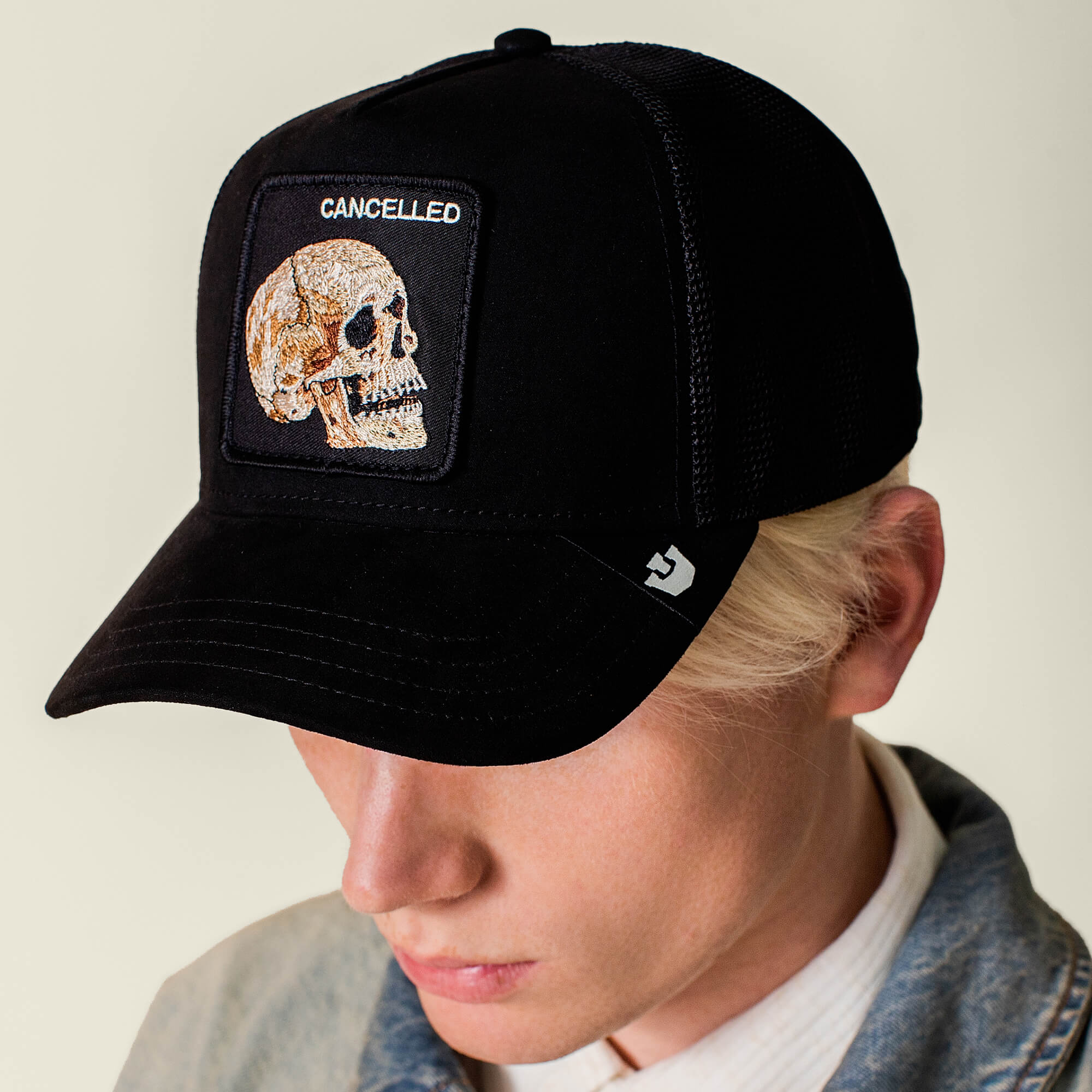 Wearing the Goorin Bros. Bold Suede Skull hat featuring a stitched skull and CANCELLED patch, paired with a light denim jacket, this person looks down.