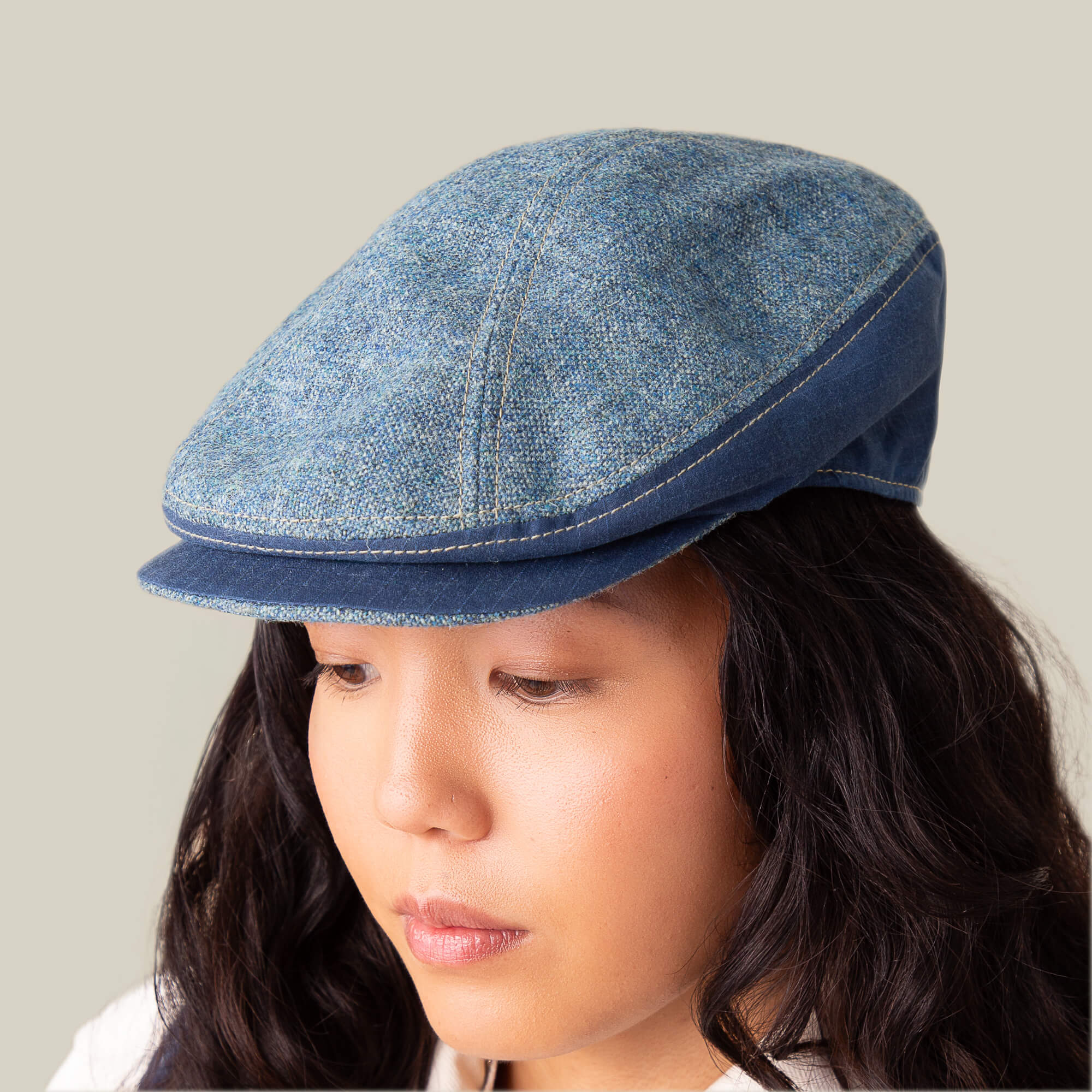 A person with long dark hair wears the Goorin Bros. Full Wattage blue tweed flatcap, looking downward against a neutral background.