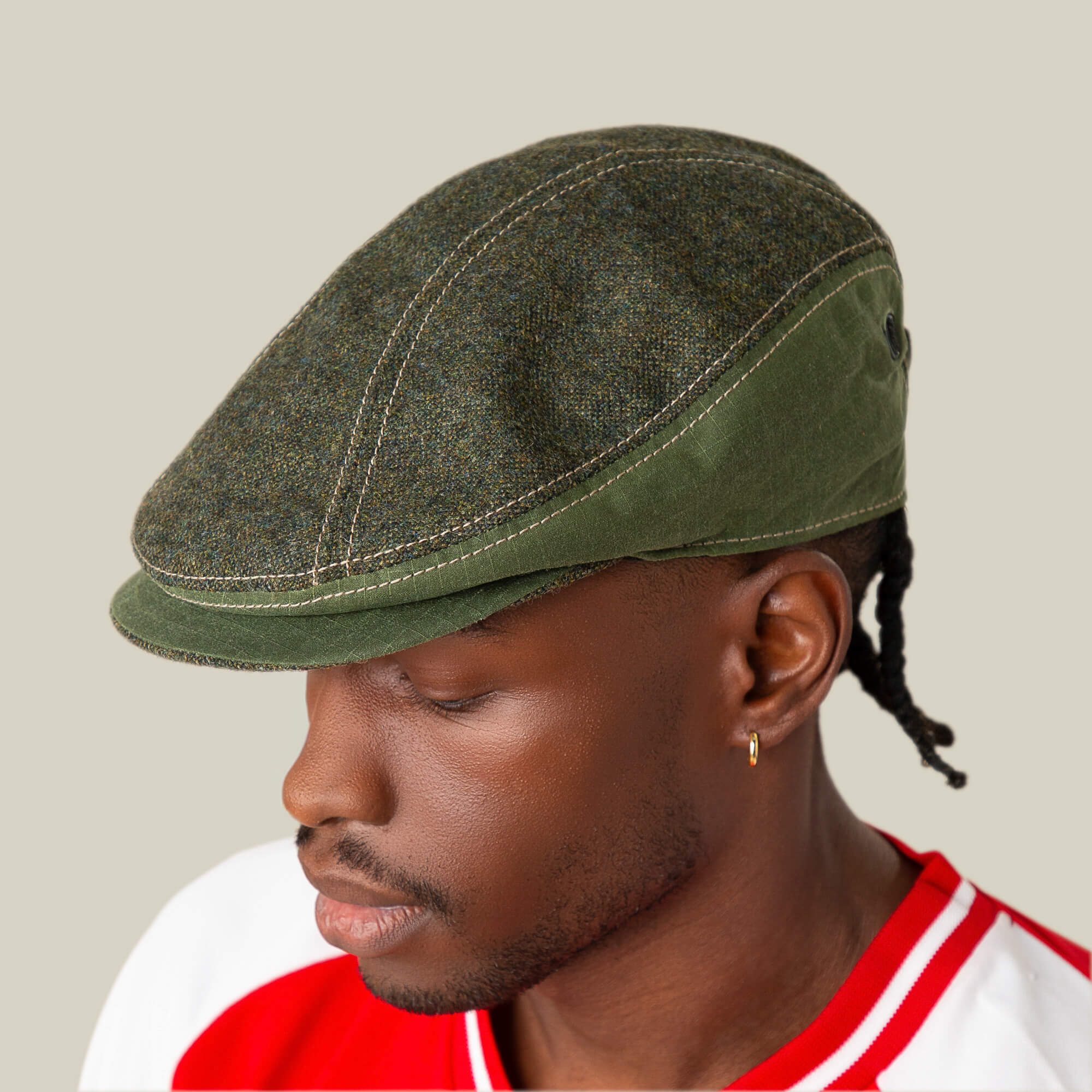 A person in Goorin Bros.' Full Wattage green flatcap and red-white shirt, shown in profile against a beige background, strikes a classic silhouette.