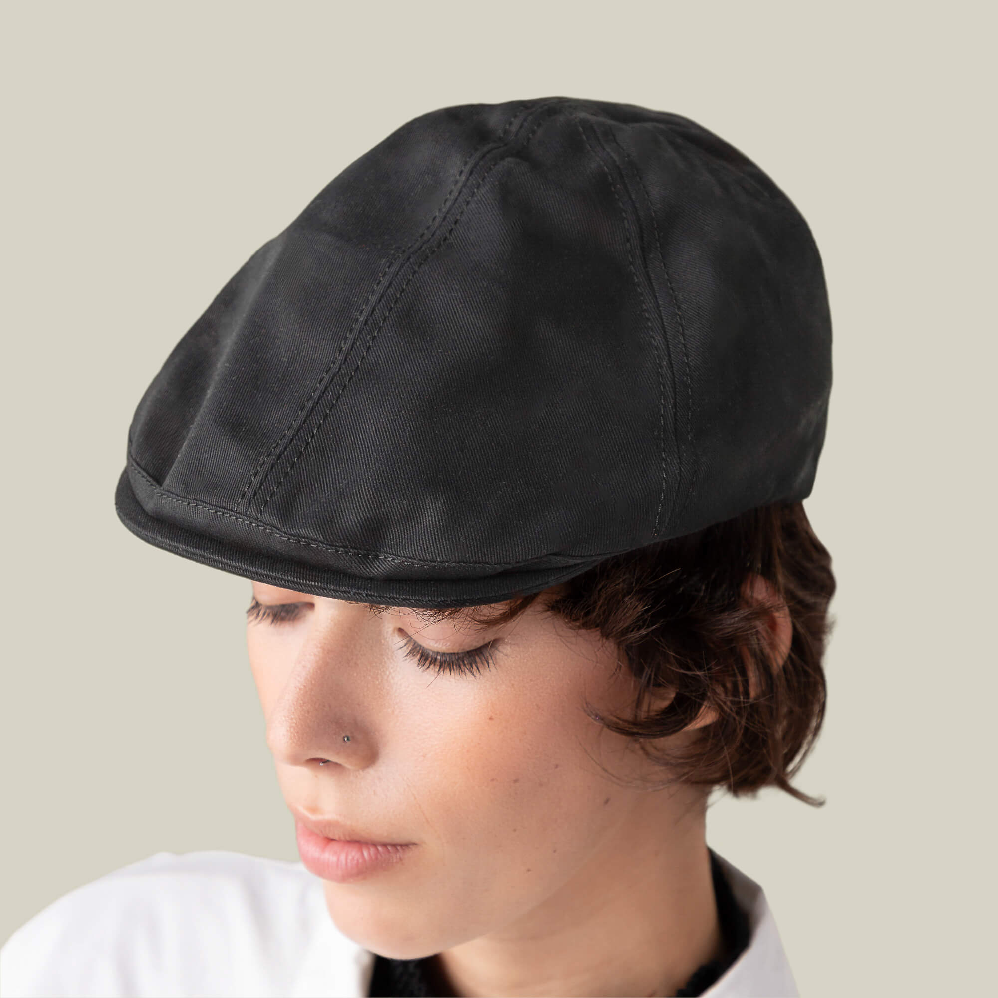 A person with short brown hair wears the Goorin Bros. Murray Way black flatcap and a 100% cotton white shirt, looking downward against a plain light background.