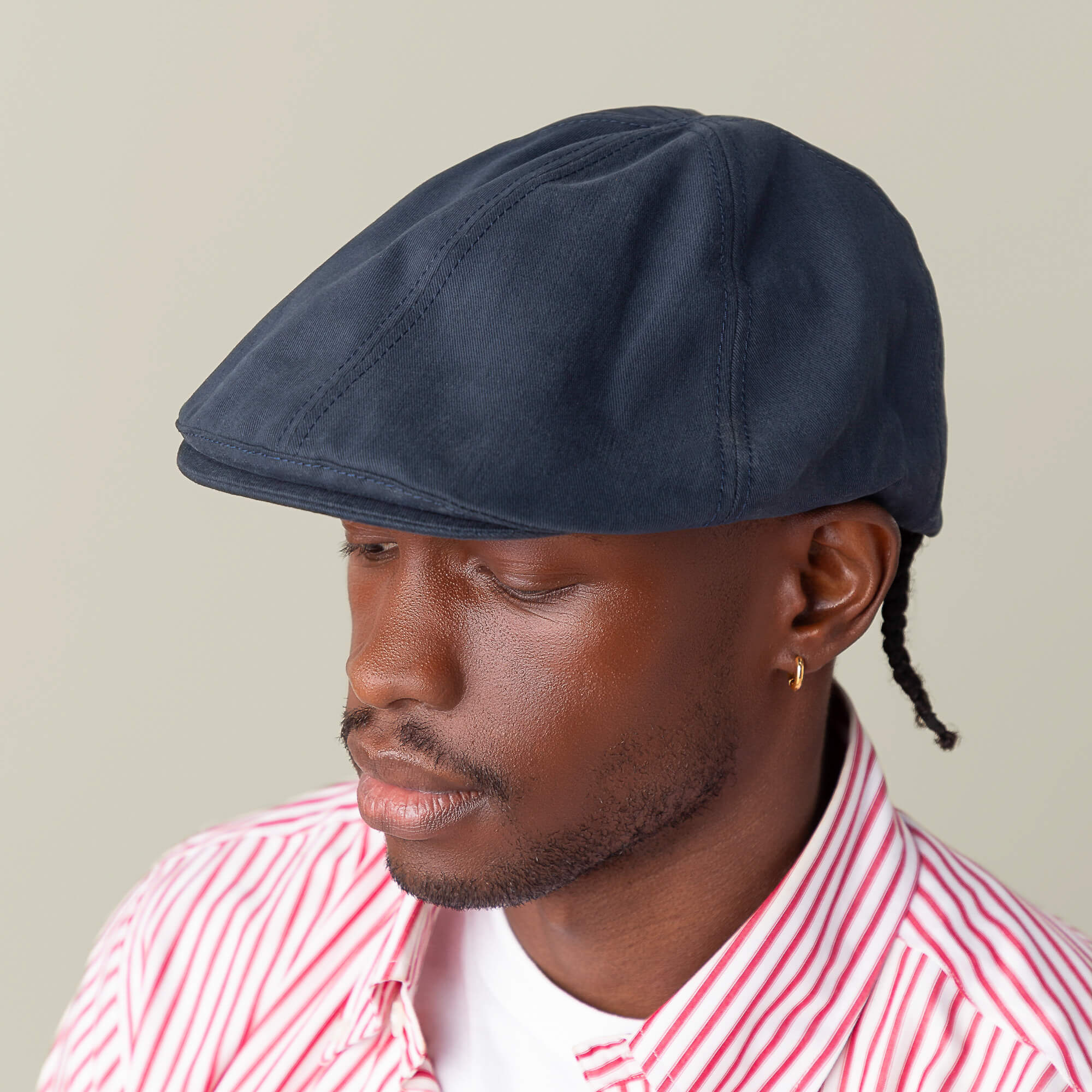 A person in the Goorin Bros. "Murray Way" navy flatcap, gold hoop earring, and red-striped shirt, looking downward against a plain background.