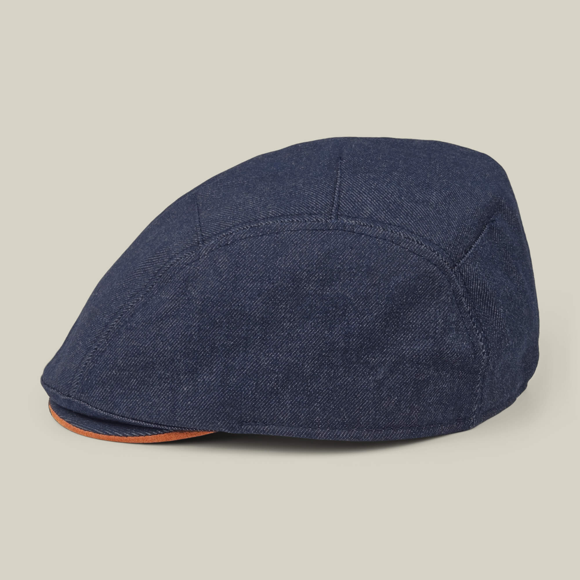 The Ashfield by Goorin Bros. is a dark blue cotton suede flat cap with visible stitching and an orange accent on the brim's edge, shown against a plain light background.