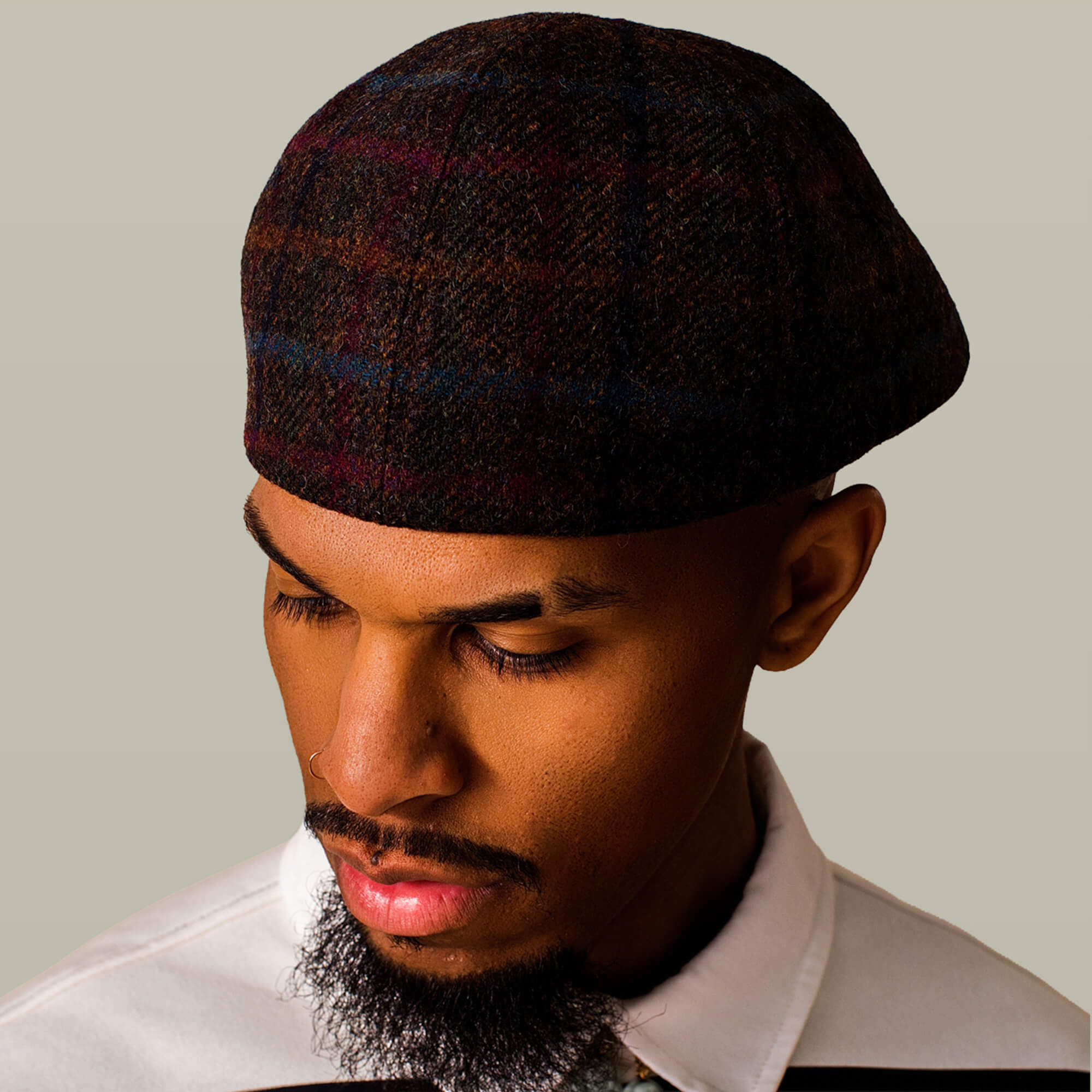 A man wearing the Goorin Bros. Cozy Benjamin Paul ivy cap in brown plaid and a white collared shirt looks down against a plain background.