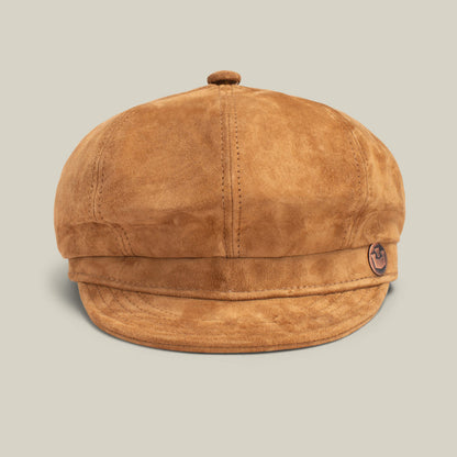The Ruthy by Goorin Bros. is a brown suede newsboy cap featuring visible stitching and a small anchor emblem on the left, styled in classic cabbie flatcap fashion against a plain light background.