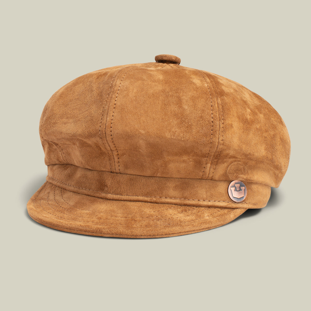 The Ruthy by Goorin Bros. is a tan cabbie-style flatcap crafted from Wolverine suede, featuring visible stitching, a small button on top, and a round metal emblem on the band, shown against a plain light background.