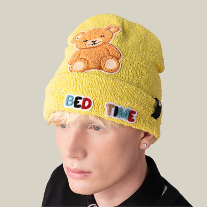 Person wearing the Goorin Bros. Nap World beanie, a yellow hat featuring a teddy bear patch and colorful "BED TIME" letters on the front, against a plain background.