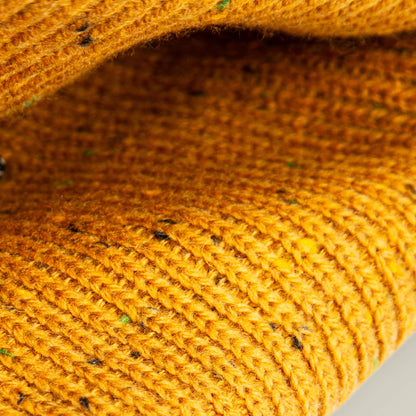 Close-up of folded, textured yellow knitted fabric with dark flecks from the No Comply by Goorin Bros.—ideal for crafting a warm, speckled beanie.