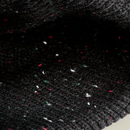 Close-up of the Goorin Bros. No Comply beanie, featuring black knit fabric with subtle white, red, and green flecks woven throughout its warm material.