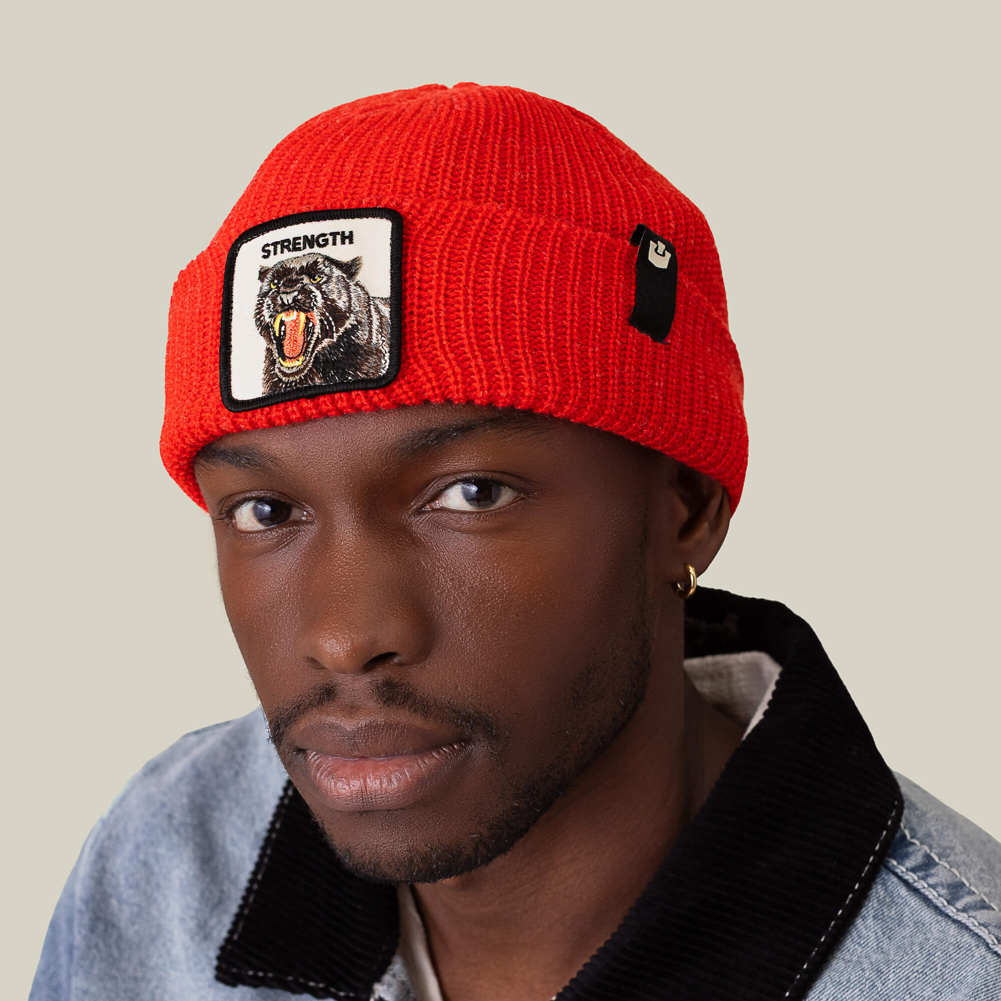 A man sports The Strength Beanie by Goorin Bros.—a red knit hat featuring a roaring bear patch and the word "STRENGTH"—paired with a light denim jacket for added warmth and style.