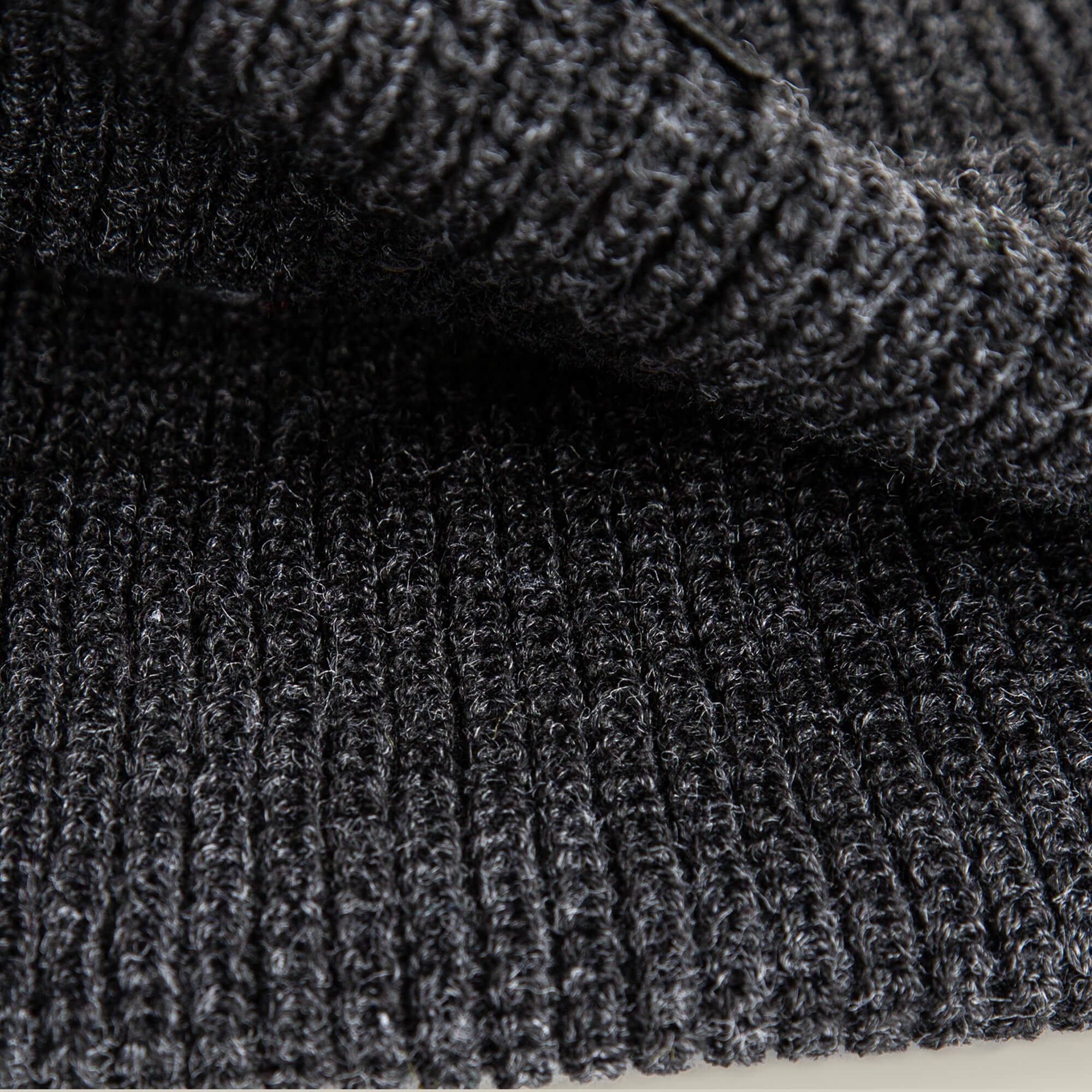 Close-up of a folded, dark gray, ribbed knit fabric highlights the texture—ideal for The Cancelled Beanie by Goorin Bros., making it a perfect choice for a charcoal knit cuff or a stylish skull patch accessory.