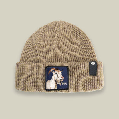 Stay warm in The Him Beanie by Goorin Bros.—a BISCUIT-colored knit with a cuff, bold goat patch, and "HIM" text on the front, plus a black tag with a white logo on the right side.