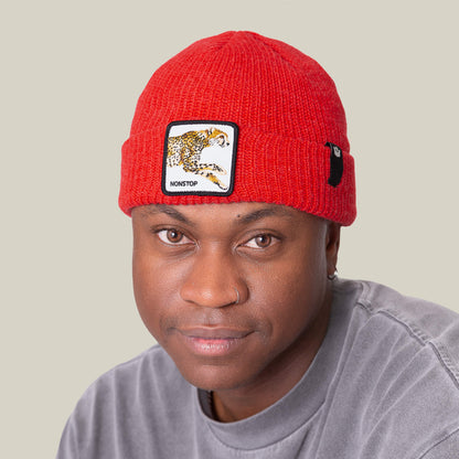 Person wearing The Nonstop Beanie by Goorin Bros.—a red knit beanie with a leopard patch—and a grey shirt, looking at the camera against a plain light background.