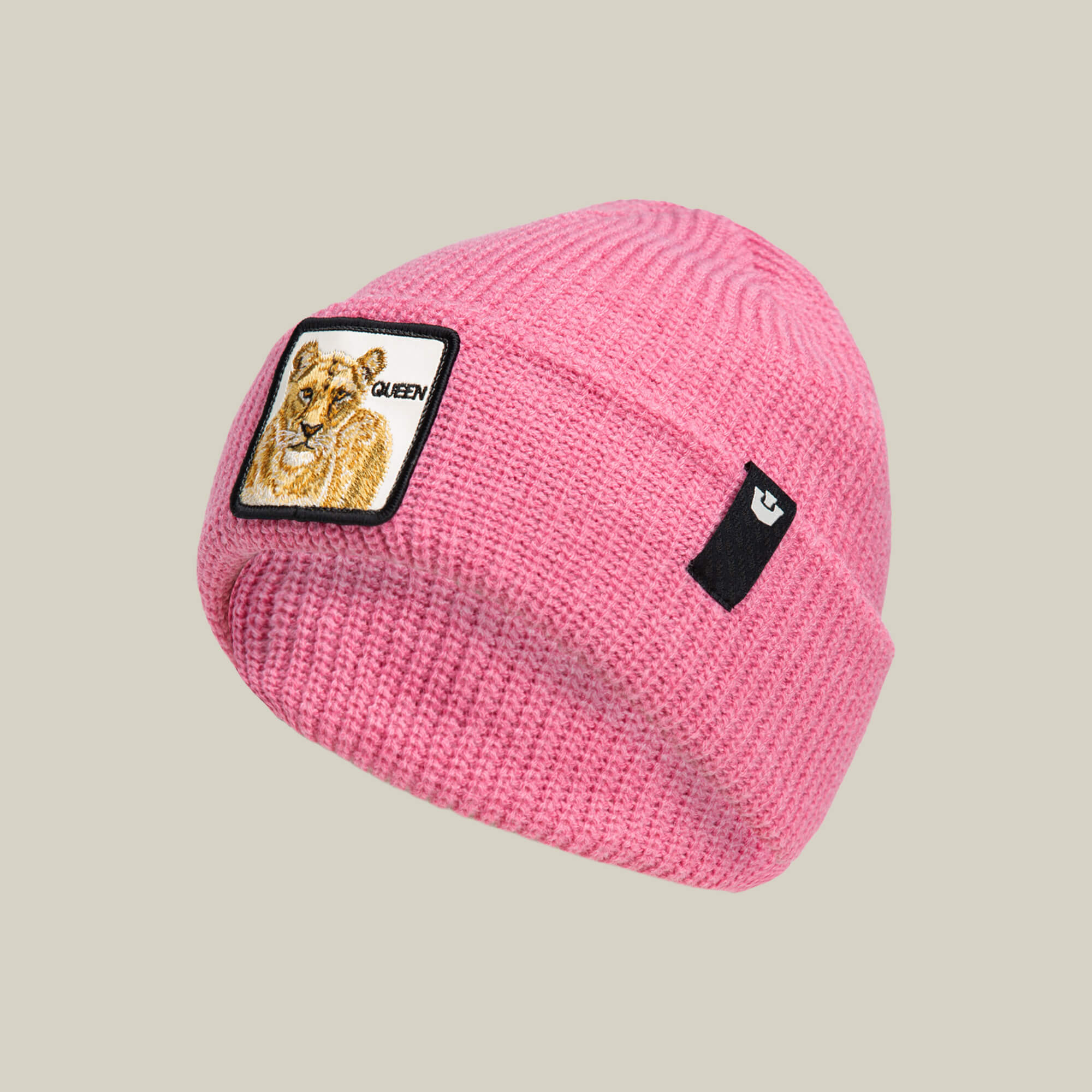 The Queen Beanie by Goorin Bros. is a pink knit hat with a lioness and "QUEEN" patch on the front, plus a small black label on the side.