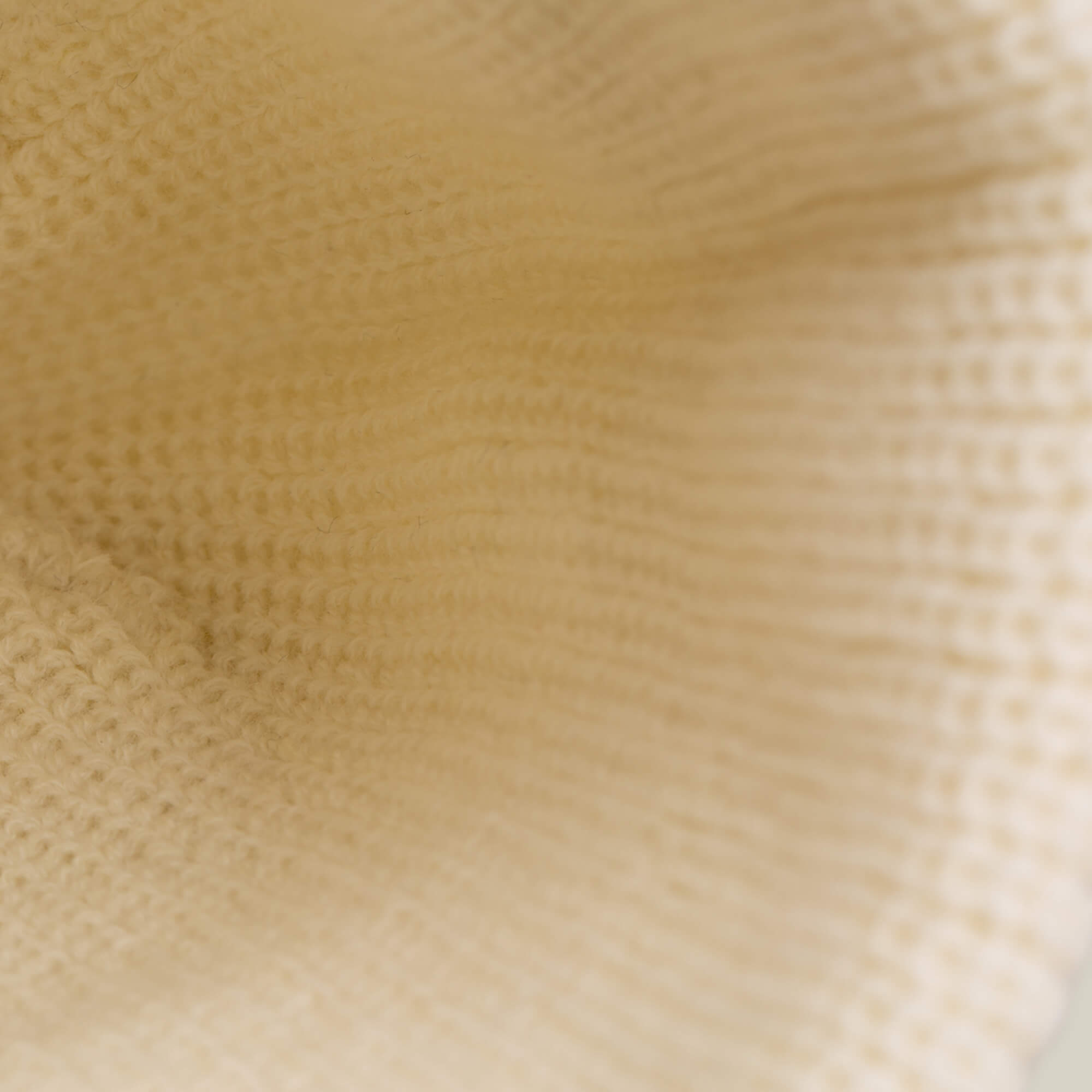 Close-up of a cream-colored knitted fabric, highlighting the texture and pattern of stitches on The Lone Wolf Beanie by Goorin Bros., featuring a signature howling wolf patch—perfect for winter.