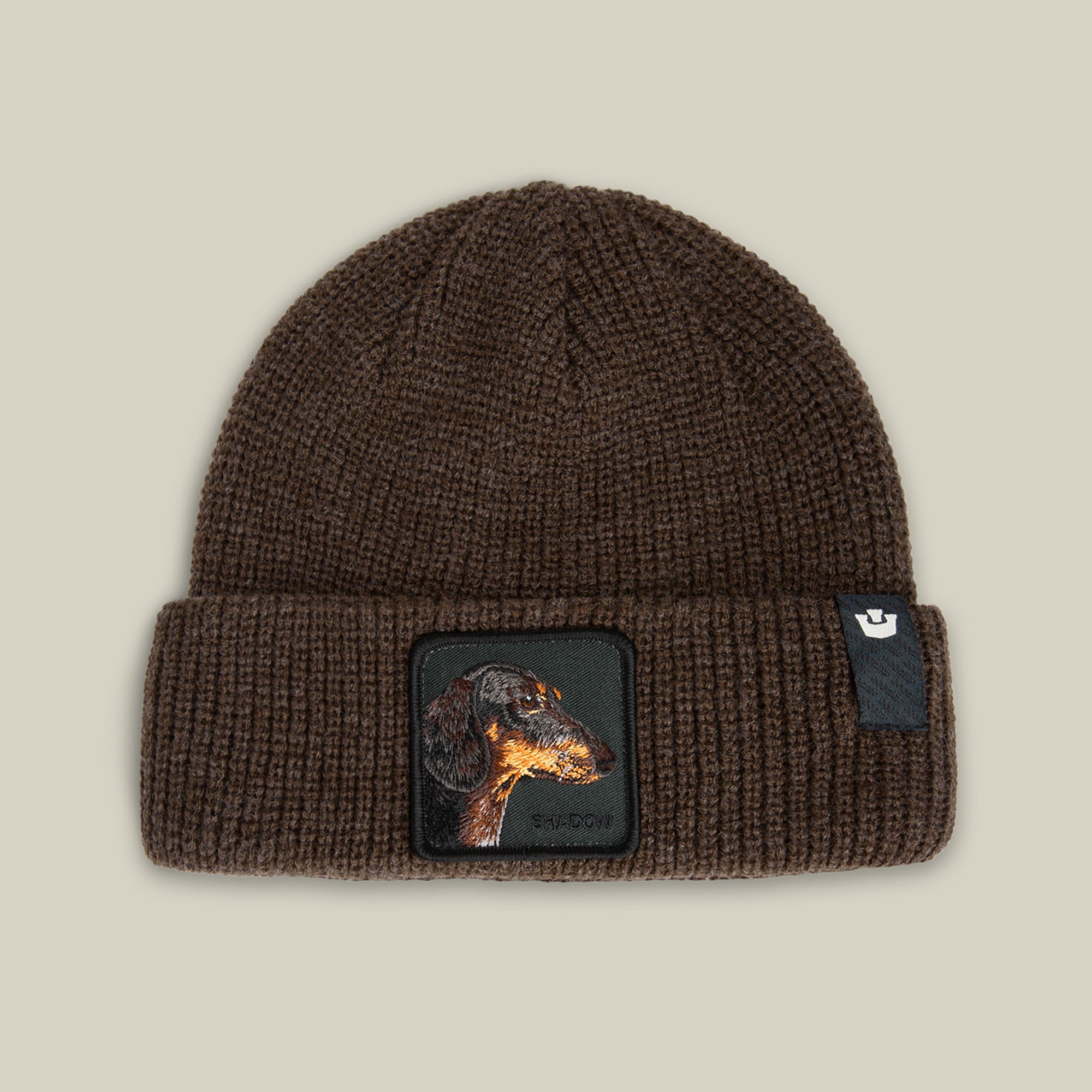 The Shadow Beanie by Goorin Bros. in GROUND features a dachshund patch and a small black tag on the folded brim.