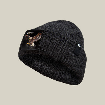 The Savage Beanie by Goorin Bros. is a warm, rugged dark knit beanie with an eagle patch, SAVAGE embroidery on one side, and a small black logo tag on the other.
