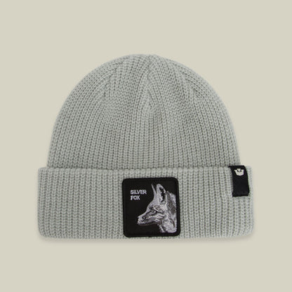 The Silver Beanie by Goorin Bros is a light gray ribbed knit beanie with a black patch featuring a silver fox illustration and text on the front, displayed against a neutral background.