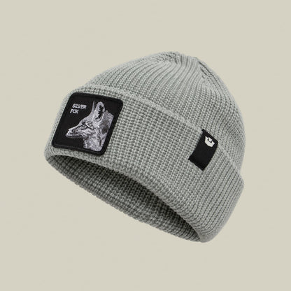 The Silver Beanie by Goorin Bros is a light gray ribbed knit beanie featuring a black embroidered patch with a silver fox illustration and text on the front, displayed against a neutral background.