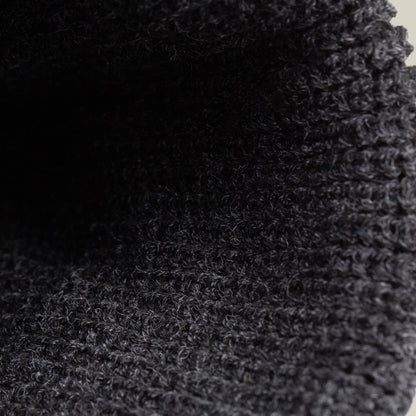 Close-up of textured, dark gray knitted fabric with visible loops and ribbed pattern, featured in The Guard Beanie by Goorin Bros.—a perfect cozy winter essential.