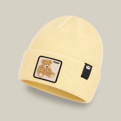 The Double Stuffed - Teddy Beanie by Goorin Bros. is a pale yellow ribbed knit beanie with a folded rib-knit cuff, featuring a teddy bear patch and a small black tag on the front—an adorable winter hat that makes the perfect go-to accessory.