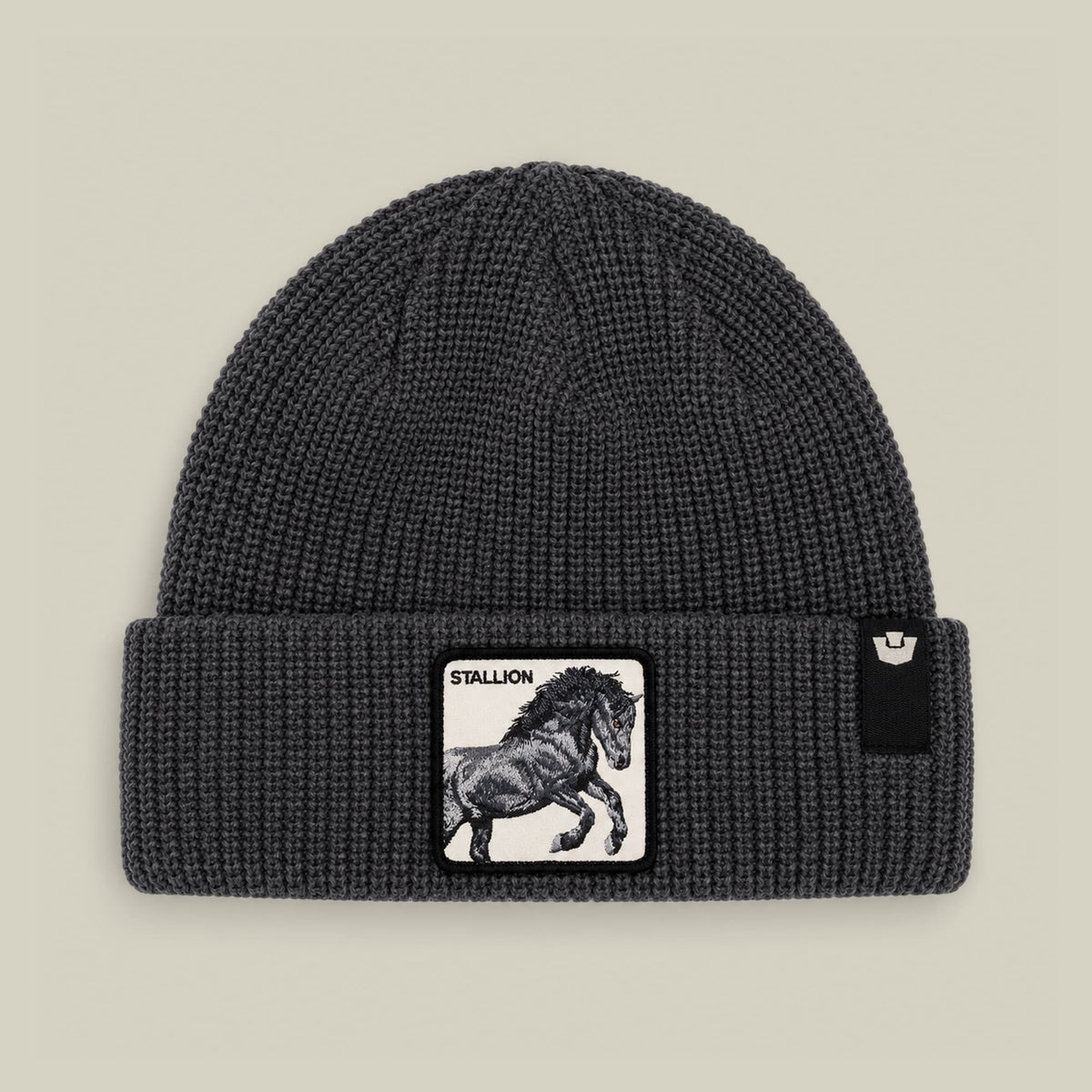 The Stallion Beanie by Goorin Bros is a charcoal gray ribbed knit beanie featuring a black and white stallion patch on the front, displayed flat against a neutral background.