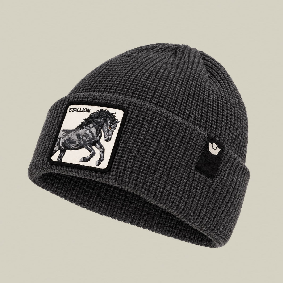 The Stallion Beanie by Goorin Bros is a charcoal gray ribbed knit beanie featuring a white patch with a black stallion illustration and text on the front, displayed against a neutral background.