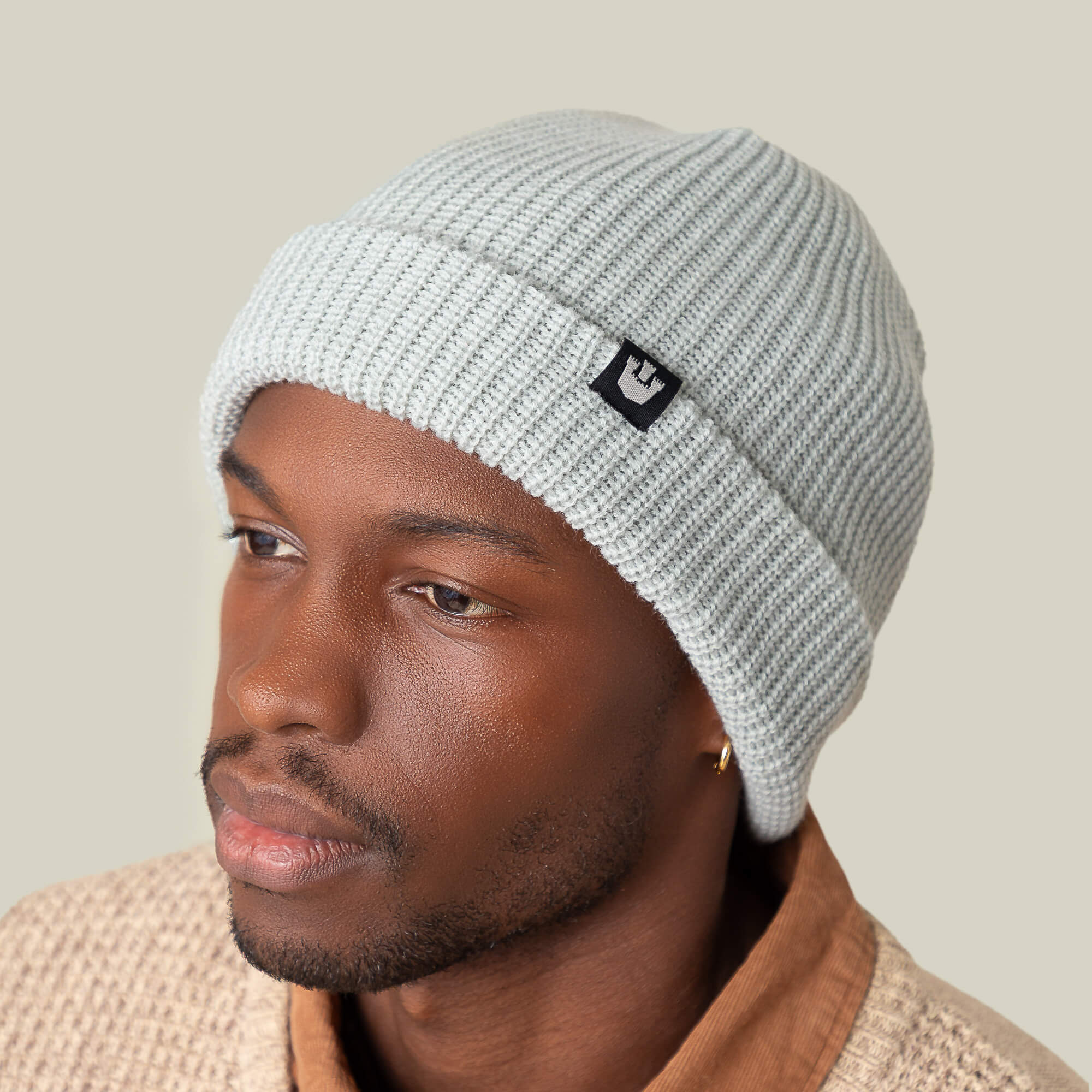 A man wears the Goorin Bros. Air to Fakie light gray beanie in lightweight poly knit and a textured beige sweater, glancing to the side against a plain background, highlighting versatile all-season style.