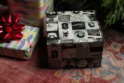 A square Goorin Gift Box by Goorin Bros., wrapped in black-and-white collage paper, sits on a patterned rug next to another present with a red bow—an ideal surprise for any headwear enthusiast.