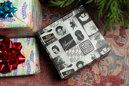 The Goorin Gift Box by Goorin Bros., wrapped in black-and-white collage paper with vintage photos and text, is perfect for headwear fans and sits next to a festive Christmas package topped with a red bow.