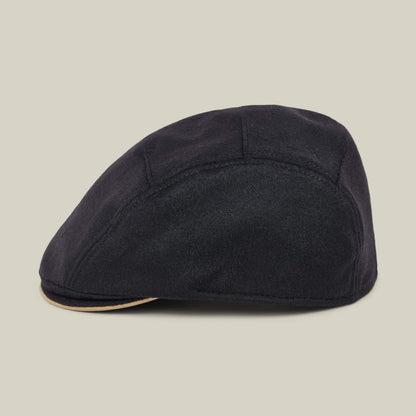 The Goorin Bros. Cornerstone is a black flat cap featuring a tan trim along the edge, handmade in New Jersey and displayed in profile against a plain light background.