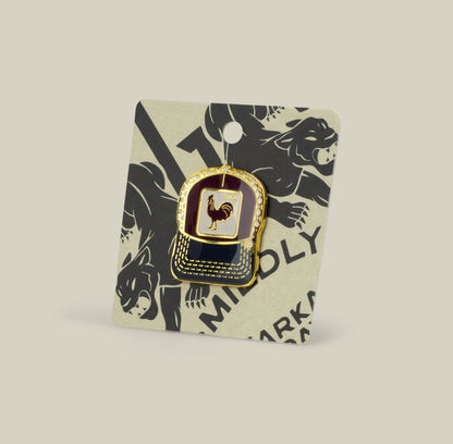 The Goorin Bros. Rooster Trucker Pin, gold and black with a rooster design, is shown on a card decorated with black animal illustrations.