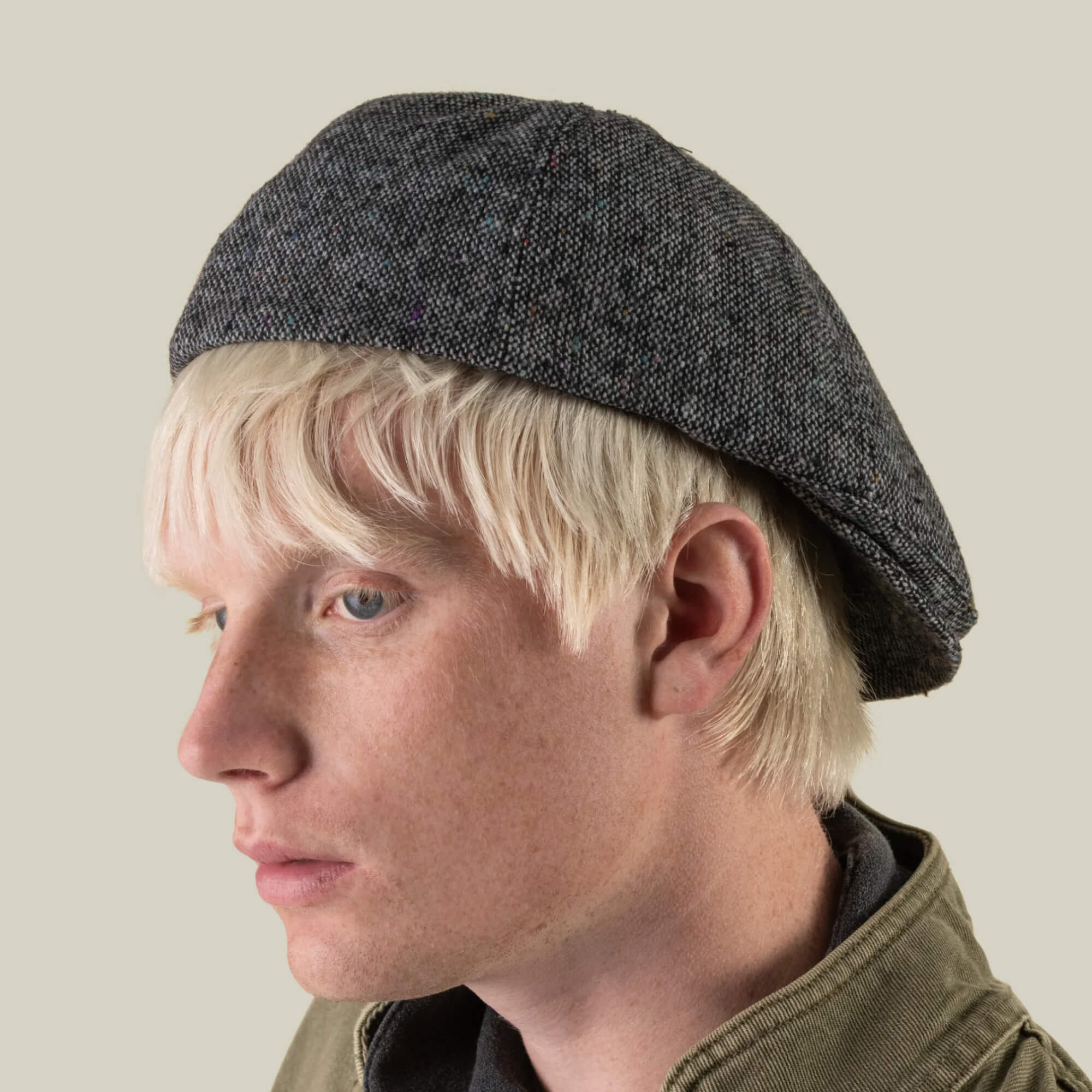 A person with light blonde hair is shown in side profile against a plain light background, wearing the Goorin Bros. Newlands digital gray beret and a green jacket.