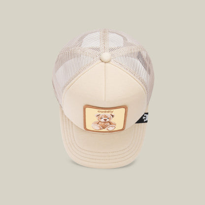 The Goorin Bros. "Cuddle Time" kids trucker cap features beige mesh and a patch with a teddy bear and "cuddly" on the front—perfect for cozy hat lovers.