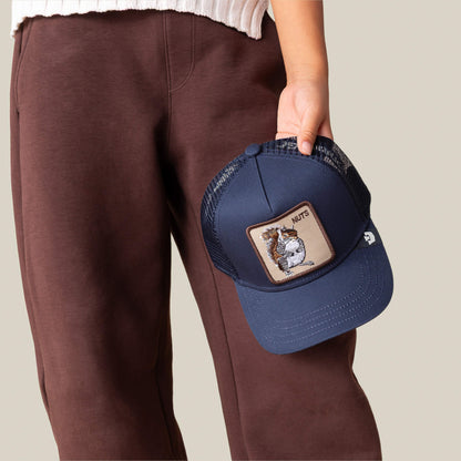 A person in brown pants and a white top holds the Goorin Bros. Nuts Mini cap—a kid-sized, navy blue mesh hat featuring a squirrel patch and the word "NUTS.