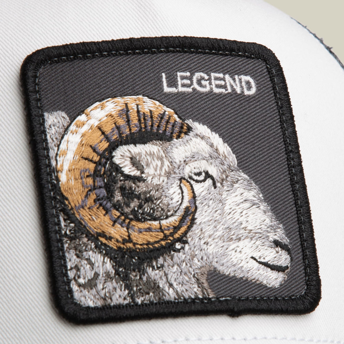 The Goorin Bros. Legend Trucker Mini features an embroidered ram head patch with gold horns and white fur on a black background, displayed as a close-up product shot.