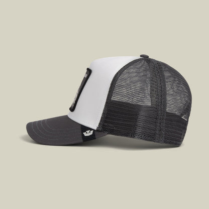 The Goorin Bros. Legend Trucker Mini is a colorblock mesh trucker hat with a white front panel and black mesh back, featuring a black cord detail and snapback closure, displayed against a neutral beige background.