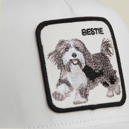 The Goorin Bros. Bestie Trucker Mini is a white and black trucker hat featuring an embroidered dog patch with "BESTIE" text, shown in a flat lay product shot on a neutral background.