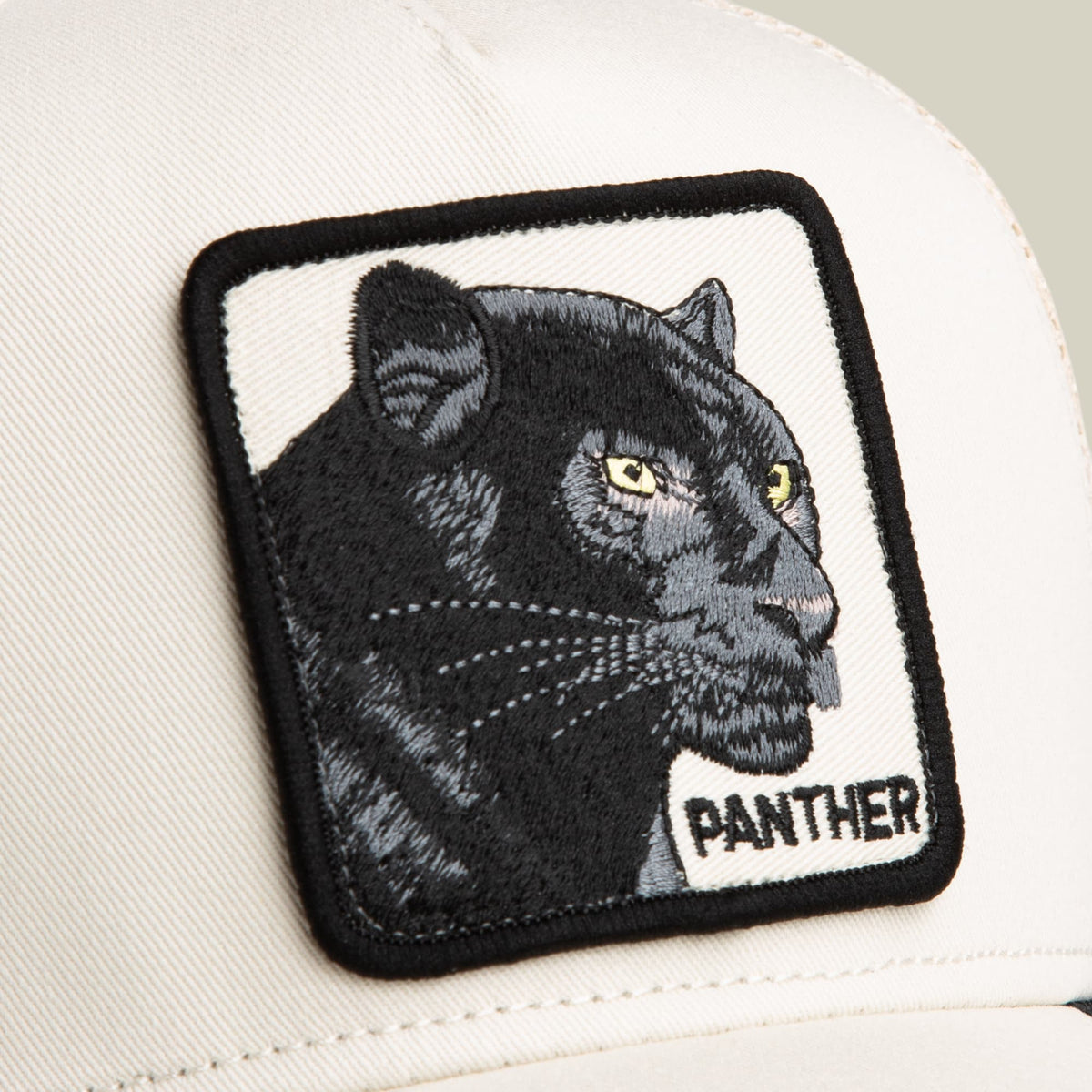 The Goorin Bros. Panther Trucker Mini is a white baseball cap with a black embroidered panther head patch featuring yellow eyes, displayed in close-up against a neutral background.