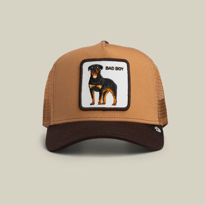 The Goorin Bros. Bad Boy Trucker Mini features a tan and brown mesh trucker cap with an embroidered patch of a black and tan dog and "Bad Boy" text on the front.