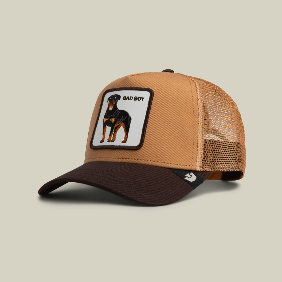 The Goorin Bros. Bad Boy Trucker Mini is a tan and black mesh trucker hat featuring an embroidered Doberman Pinscher patch with "Bad Boy" text on the front, displayed on a neutral background.