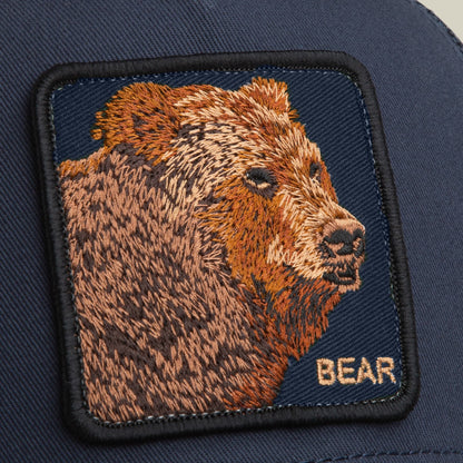 The Goorin Bros. Bear Trucker Mini features a navy blue trucker hat with an embroidered bear head patch in brown and tan tones on the front, displaying detailed wildlife imagery and the word BEAR embroidered below.