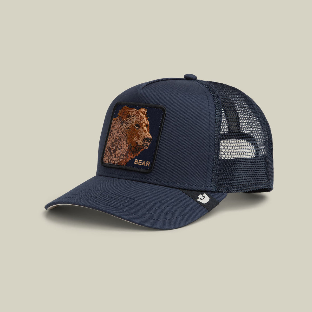 The Goorin Bros. Bear Trucker Mini is a navy blue mesh trucker hat featuring a brown embroidered bear patch on the front and a small logo detail on the side, photographed against a neutral background.