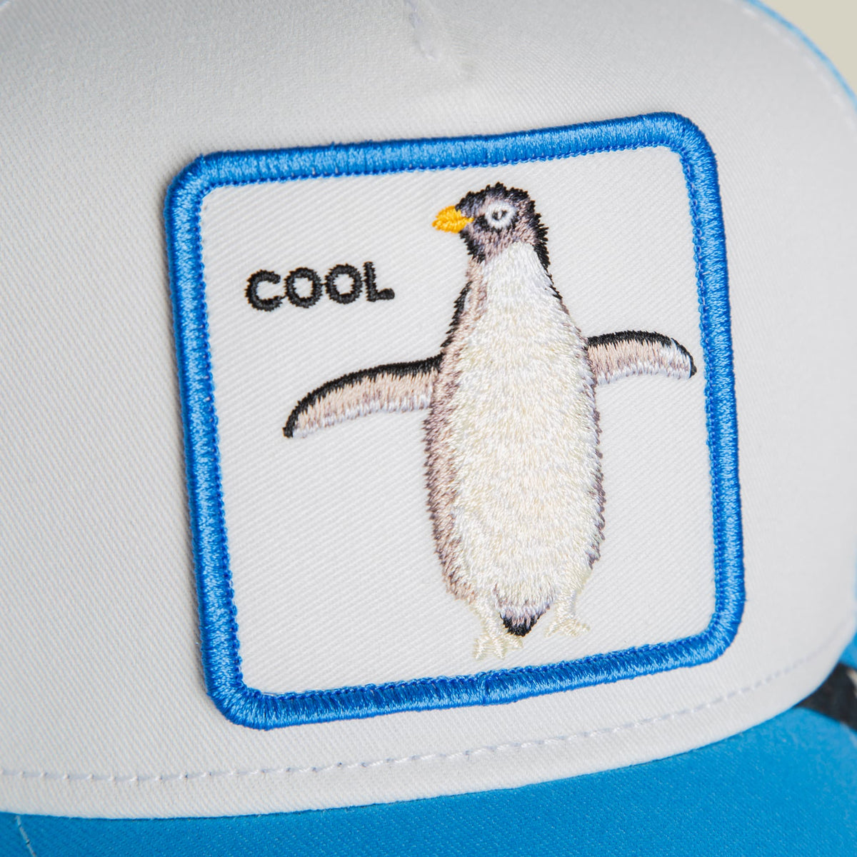 The Goorin Bros. Cool Penguin Mini is a blue and white trucker hat featuring an embroidered penguin patch with the word "cool" on the front panel, displayed against a neutral background.