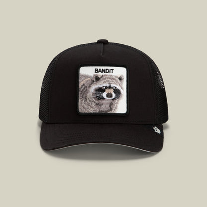 The Goorin Bros. Bandit Trucker Mini is a black mesh snapback cap featuring a white embroidered patch with a detailed raccoon illustration and "BANDIT" text on the front.