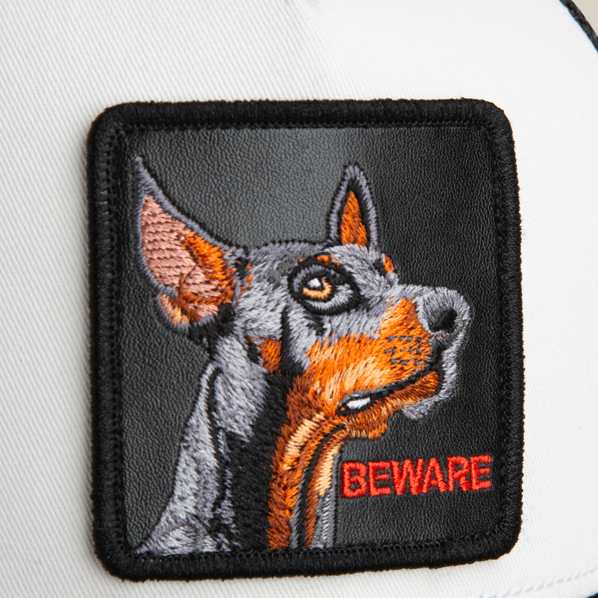 Add an eye-catching touch to your favorite accessory with the Goorin Bros. Beware Trucker Mini—a white fabric patch featuring an embroidered Doberman’s head and the word BEWARE stitched in red at the bottom right corner, perfect for customizing your hat or showing off some attitude.