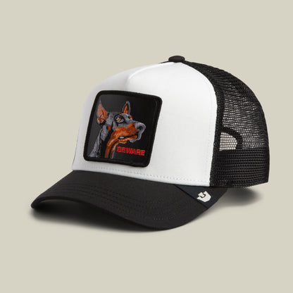 The Beware Trucker Mini by Goorin Bros. is a black and white mesh trucker mini hat featuring an embroidered patch with a striking Doberman and the word “BEWARE” in bold red letters on the front.
