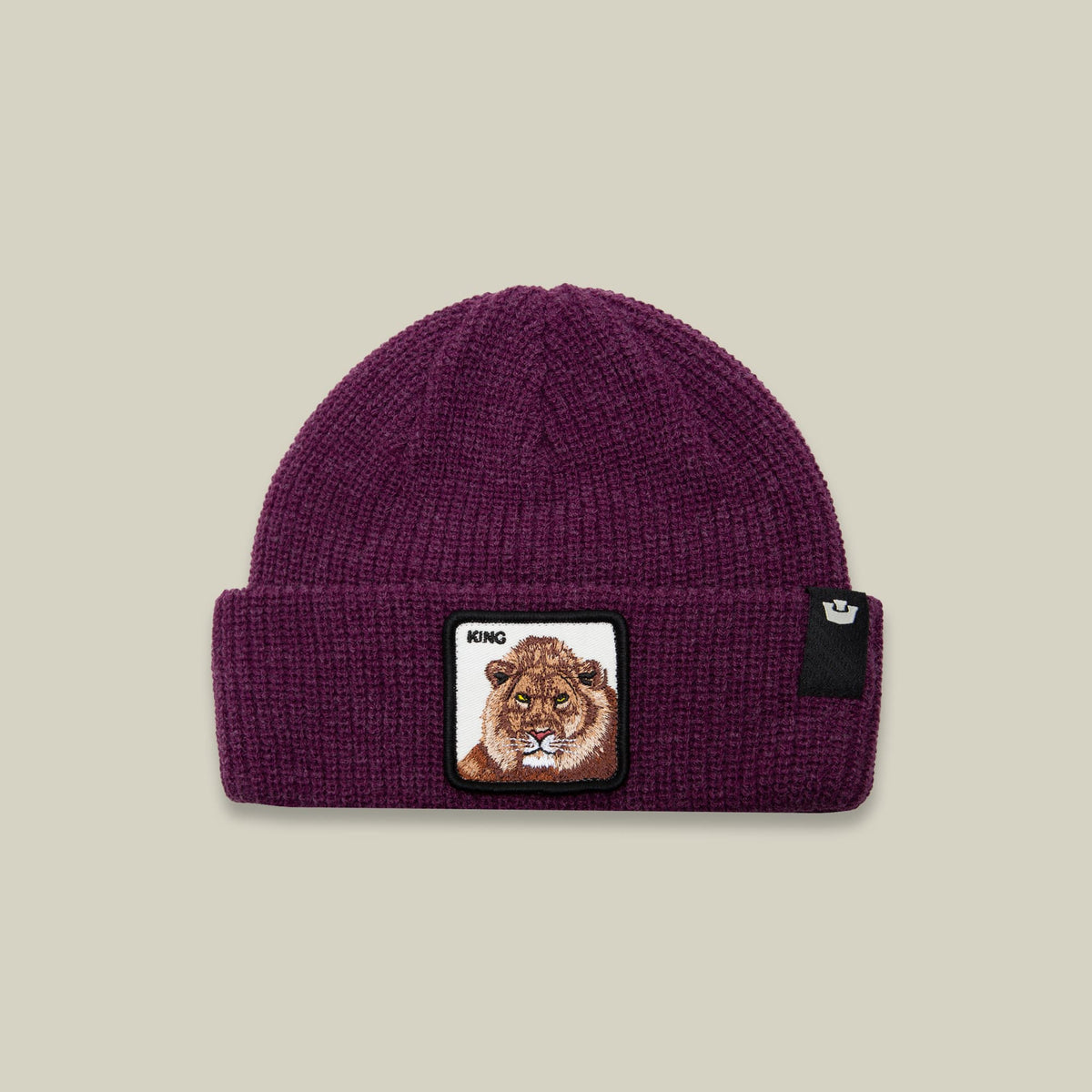 The King Beanie Mini by Goorin Bros is a burgundy ribbed knit beanie featuring an embroidered lion patch with "KING" text on the front, displayed against a neutral studio backdrop.